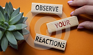 Observe your Reactions symbol. Concept word Lets do this on wooden blocks. Businessman hand. Beautiful orange background with