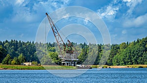 Obsolete floating crane is moored to a pier off the coast of a wooded island in Gulf of Finland. Summer sunny day