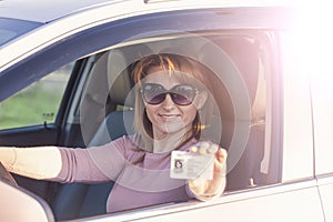 Obtaining a driverâ€™s license, a beautiful woman in sunglasses at the wheel demonstrates a new driverâ€™s license. Young woman