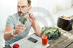 Occupied curious man sitting and examining a broccoli.