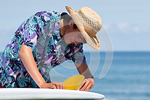 Ocean background with a Asian / Japanese boy putting a yellow fin into a surfboard.