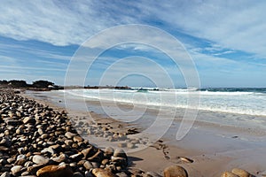 Ocean beach with large stones and sand under a blue sky and clouds