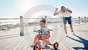 Ocean, bicycle and happy father with girl excited after learning, teaching and helping kid ride bike. Black family, love