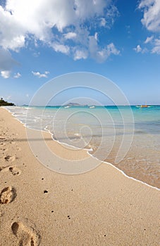 Ocean, boat and blue sky for footprints, sand and rocks in shore for peace and tranquility. Seaside, waves and summer