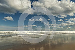 ocean coast on a sunny day with fluffy clouds. Reflection of the sky in the water on the shore. Atlantic coast