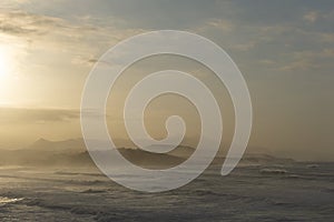 Ocean coast at sunset with waves breaking and mountains in silhouette behind