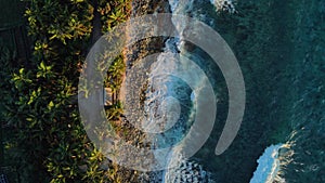 Ocean coastline with house, ocean waves and sunrise or sunset tones at tropical island. Aerial top down view