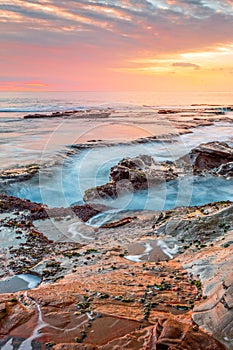 Ocean flowing into coastal channels eroded into rock and a stunning sunrise
