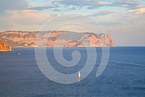 Ocean landscape and mountain on background. Cloudy sky and yacht floating in calm sea. Nature and seascape view concept