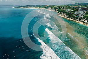 Ocean with perfect waves and coastline with hotels on Impossibles beach in Bali. Aerial view of tropical island