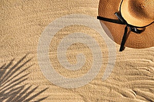 Ocean or sea shore, wicker hat lying on the sand, palm leaf shadow next to footprint.