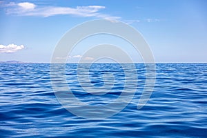 Ocean sea water surface deep blue, calm with ripple, small cloud on blue sky background