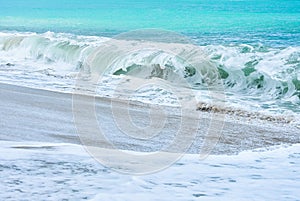 An ocean shorebreak in front view. Big beautiful green blue wave splashing with backwave and ready to break out. White foam