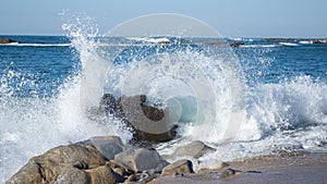 Ocean spray splashing into the air as waves splash over rocks on the beach