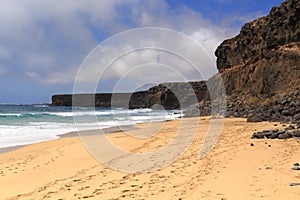 The ocean, stone cliff, blue sky and sandy beach