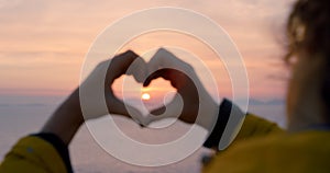 Ocean sunset, heart hands sign and woman with wind in hair on travel adventure for peace, freedom and calm fresh air