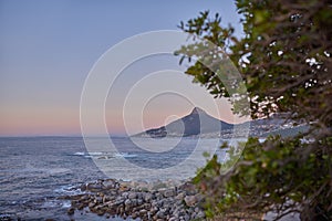 Ocean view of sea water on rock beach, mountains and twilight sky with copy space of Lions Head in Cape Town, South