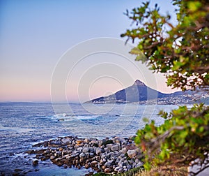 Ocean view on a shallow rocky shoreline with Lions Head, Table Mountain National Park in Cape Town, South Africa in the