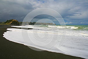 Ocean water foam on black stones and sand at Whirinaki Beach, Hawke`s Bay, Napier, New Zealand