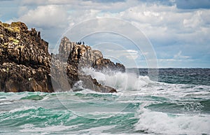 Ocean water splash on rock beach with beautiful sky and clouds. Sea wave splashing on stone at sea shore on winter. Sea waves lash