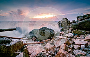 Ocean water splash on rock beach with beautiful sunset sky and clouds. Sea wave splashing on stone at sea shore on summer. Nature