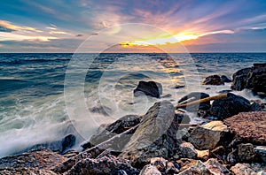 Ocean water splash on rock beach with beautiful sunset sky and clouds. Sea wave splashing on stone at sea shore on summer. Nature