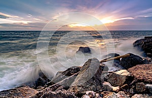 Ocean water splash on rock beach with beautiful sunset sky and clouds. Sea wave splashing on stone at sea shore on summer. Nature