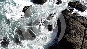 Ocean water swirls amongst rocks as seen from above as wave arrives