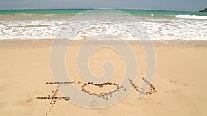 Ocean wave approaching words I love you written in sand on beach