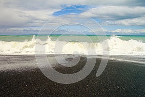 Ocean wave contrasting with black stones beach Whirinaki beach near Napier, New Zealand