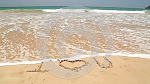 Ocean wave covering words I love you written in sand on beach