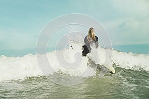 Ocean, wave and splash with surfer woman in wetsuit for sports, fitness or exercise in summer from back. Blue sky, sea