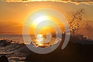 An ocean wave splashes off rocks in golden sunset