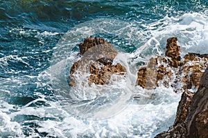 Ocean waves braking at coastline rocks covering them in white sea foam