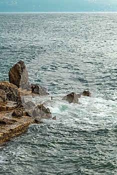 Ocean waves braking at coastline rocks covering them in white sea foam