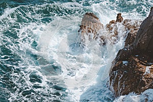 Ocean waves braking at coastline rocks covering them in white sea foam