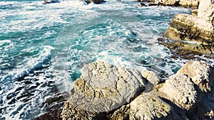 Ocean waves breaking on rocks at coast, aerial view seashore in stormy and sunny weather, Cyprus Nature