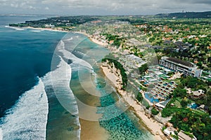 Ocean with waves and coastline with hotels on Impossibles beach in Bali. Aerial view of tropical island