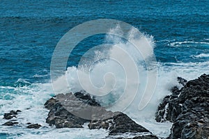 Ocean waves crashing against black rocks on coast