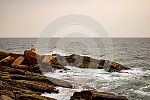 Ocean, waves crashing against rocks and a man sitting on the stone in Sri Lanka