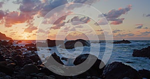 Ocean waves crashing against stone rock cliffs at north of Tenerife Island. Waves breaking on black stones at sunset