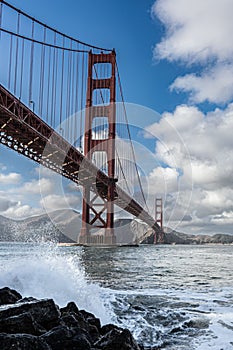 Ocean waves crashing into rocks at the shore under Golden Gate Bridge, San Francisco, California
