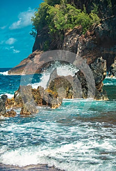 Ocean waves crashing on the rocky island coast. Splashing ocean waves and stones. Red Sand Beach, Maui in in Hawaiian.