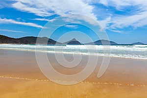 Ocean waves, forested rocky outcrops and blue sky.