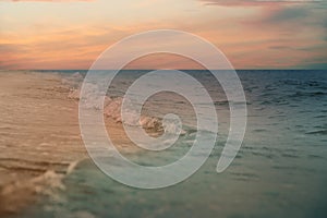 Ocean waves rolling on sandy beach under sky with clouds at sunset