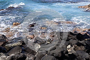 Ocean waves splashing upon black volcanic rock coastline on the Hawaiian Island of Kona, Hawaii, USA