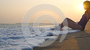 Ocean waves washing over tanned female body. Cute girl lying on the beach in the waves at sunset time. Beautiful young