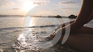 Ocean waves washing over tanned female feet at sunset. Beautiful young woman relaxing on sea shore during summer