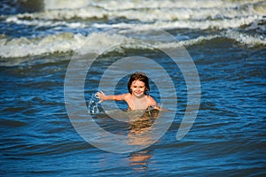 Ocean wawes on the background. Kid swimming in sea with wawes. Little boy playing in outdoor jumping into water on photo