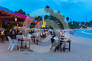 Oceanfront restaurant with lights and tables on a sandy beach